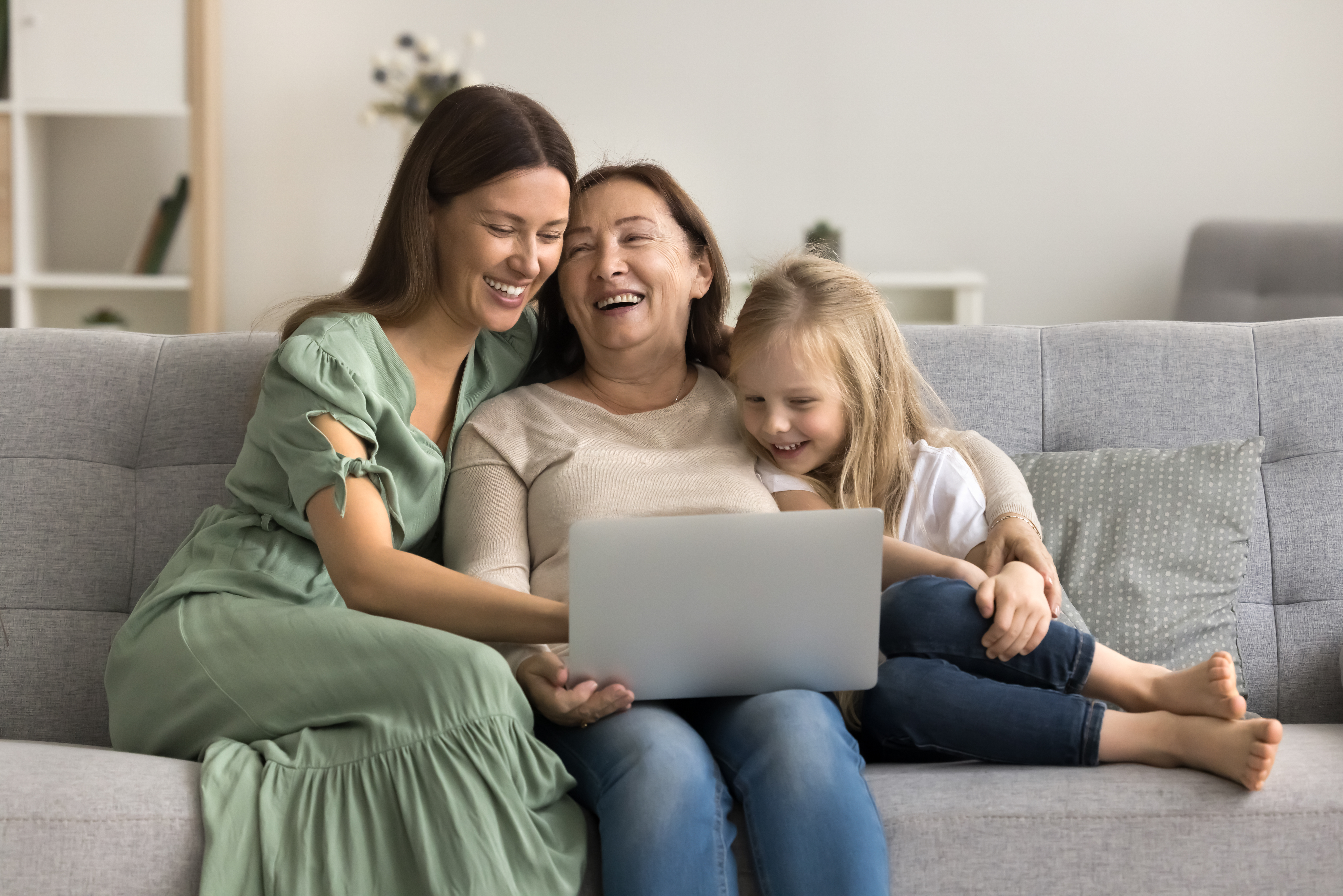 Cheerful mom, grandma and child using laptop together on sofa