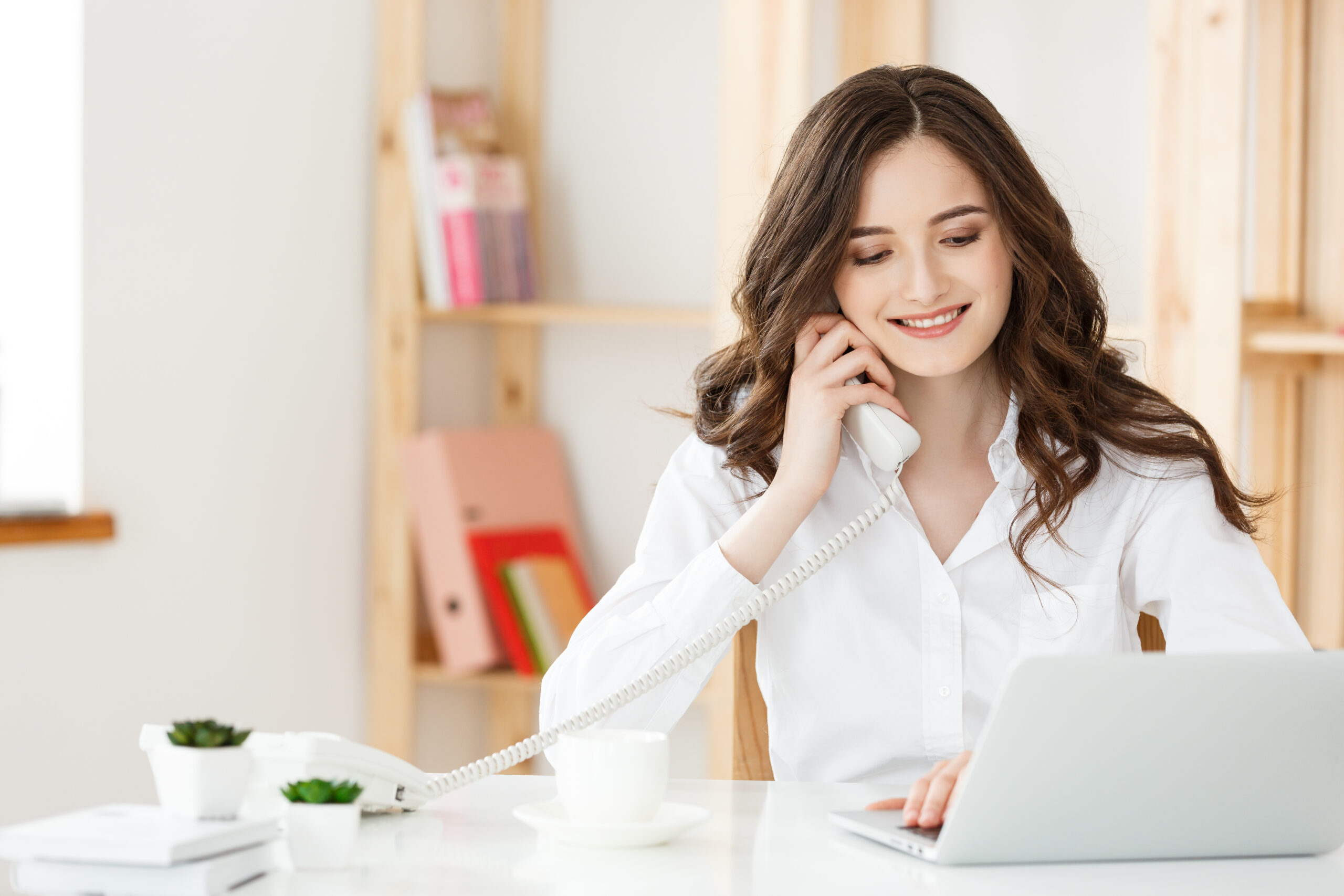 Smiling young woman making notes while talking with custumer on the phone at the call center